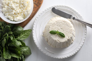 Fresh ricotta (cream cheese) with basil and knife on white wooden table, flat lay