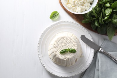 Photo of Fresh ricotta (cream cheese) with basil and knife on white wooden table, flat lay. Space for text