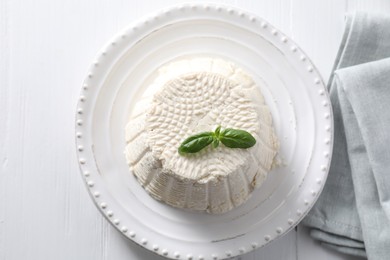 Photo of Fresh ricotta (cream cheese) with basil on white wooden table, top view