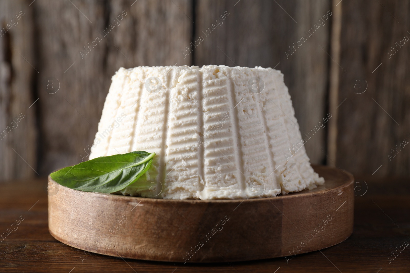 Photo of Fresh ricotta (cream cheese) with basil on wooden table, closeup