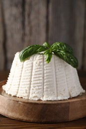 Fresh ricotta (cream cheese) with basil on wooden table, closeup