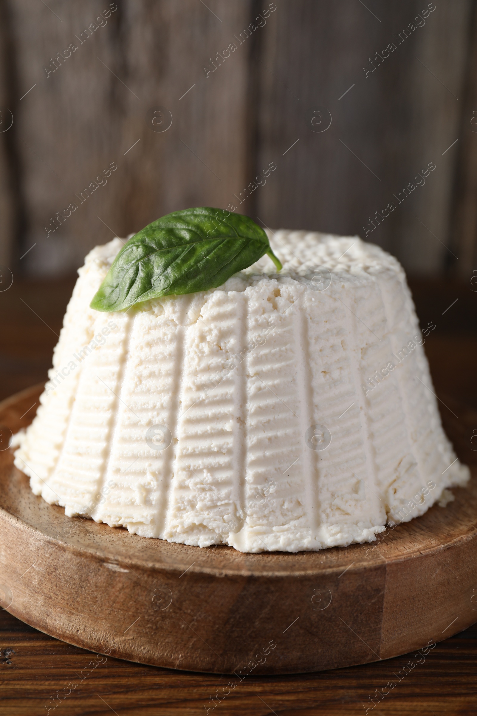 Photo of Fresh ricotta (cream cheese) with basil on wooden table, closeup