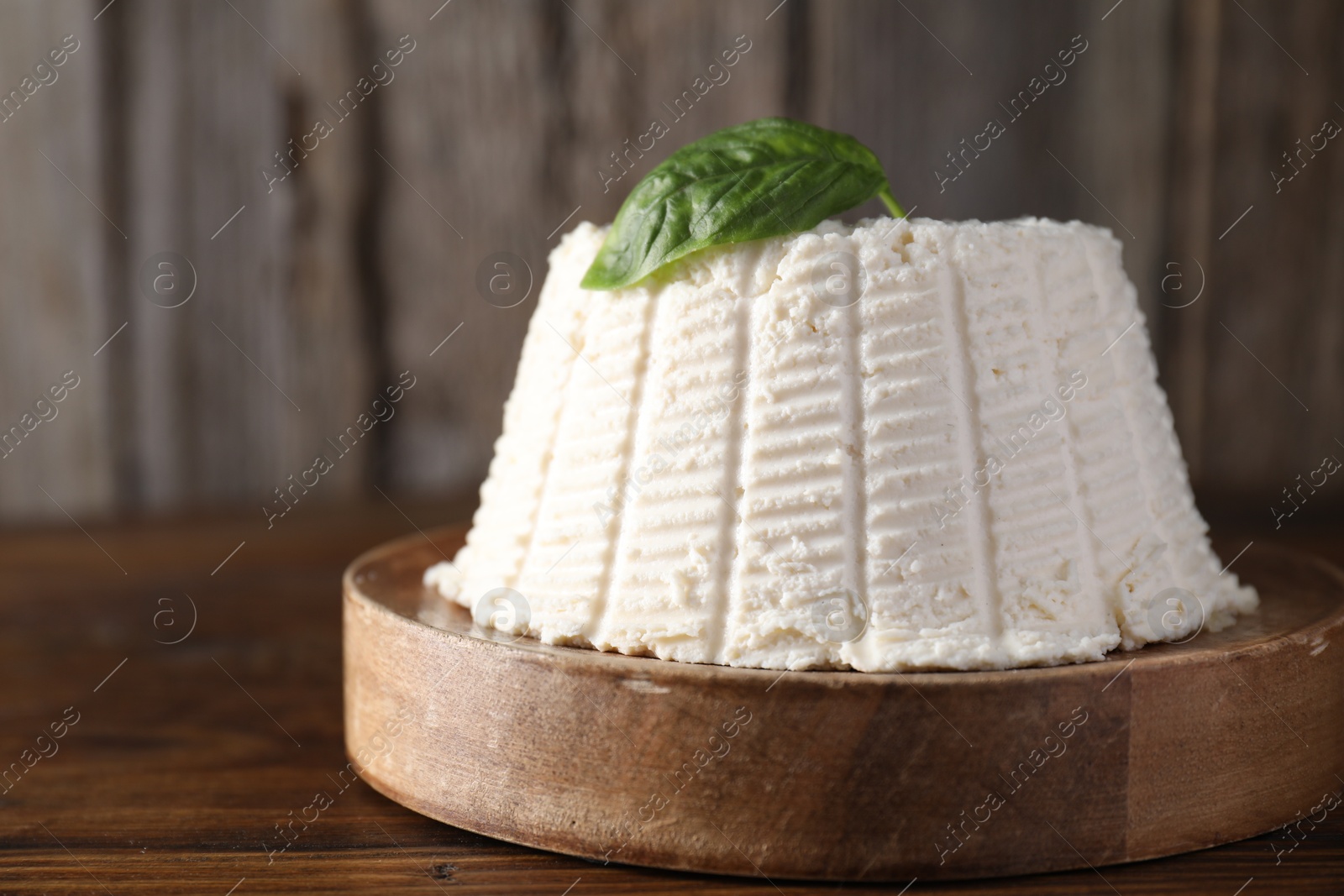 Photo of Fresh ricotta (cream cheese) with basil on wooden table, closeup