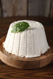 Fresh ricotta (cream cheese) with basil on wooden table, closeup