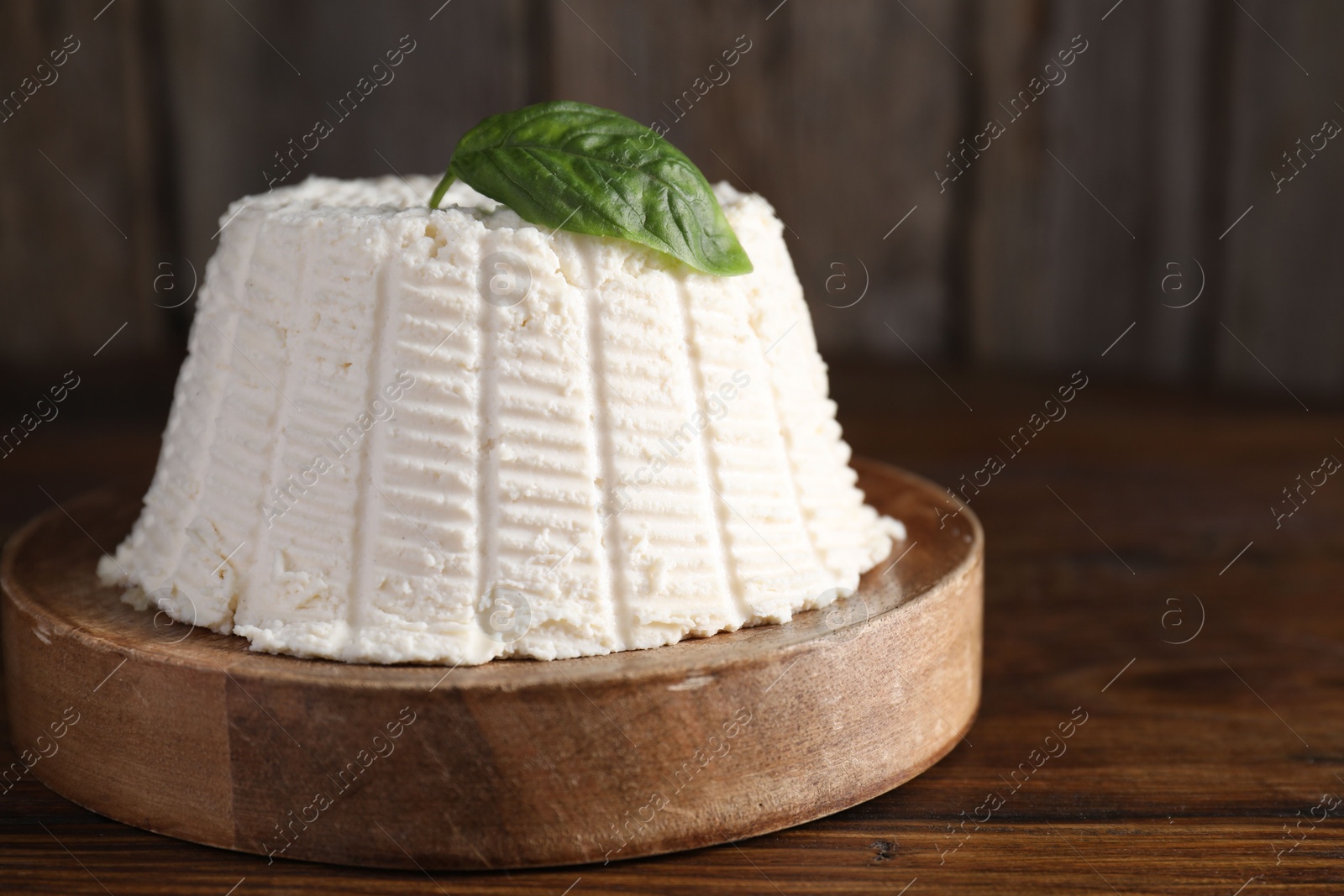 Photo of Fresh ricotta (cream cheese) with basil on wooden table, closeup