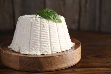 Fresh ricotta (cream cheese) with basil on wooden table, closeup