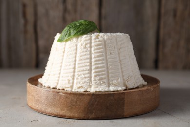 Photo of Fresh ricotta (cream cheese) and basil on light grey table, closeup