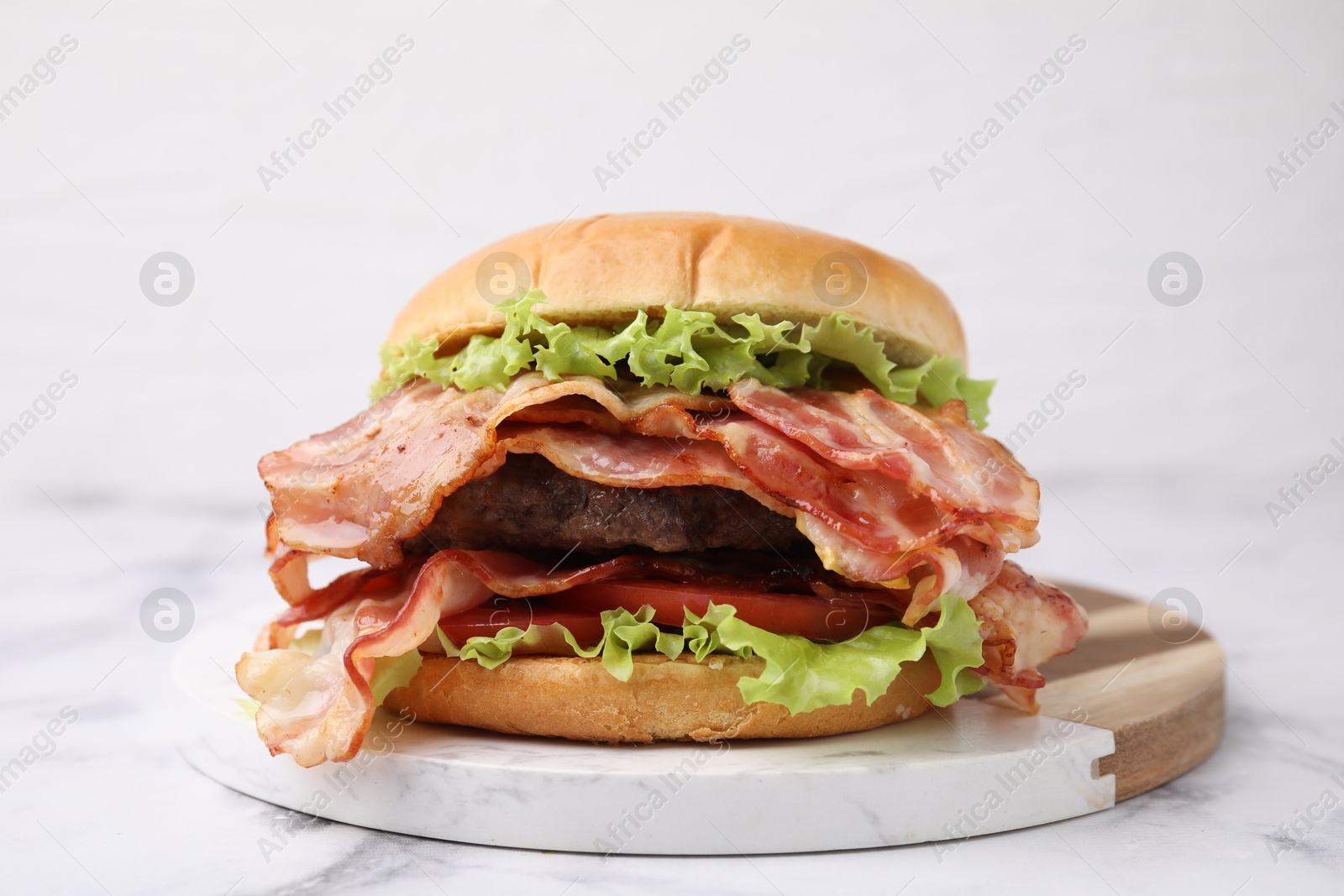 Photo of Delicious burger with bacon, patty and tomato on white marble table