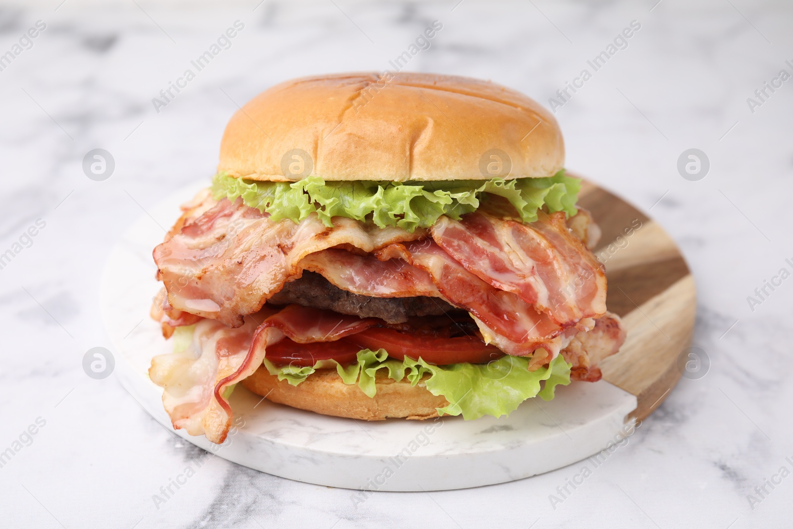 Photo of Delicious burger with bacon, patty and tomato on white marble table