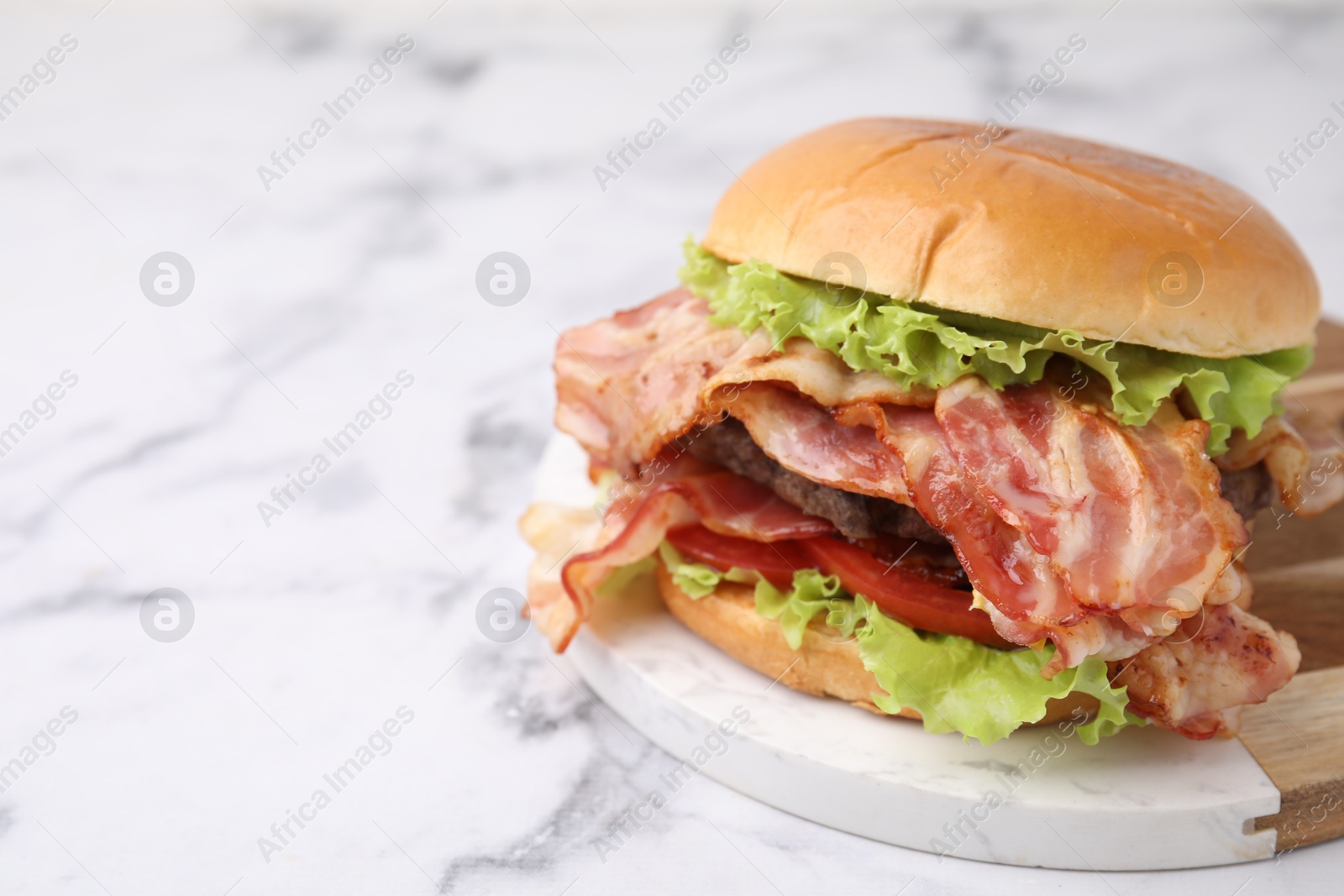 Photo of Delicious burger with bacon, patty and tomato on white marble table, space for text