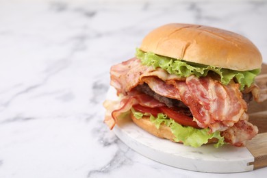 Delicious burger with bacon, patty and tomato on white marble table, space for text