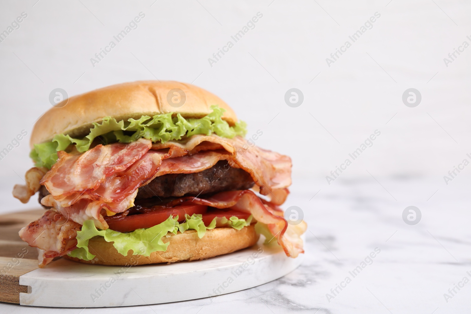 Photo of Delicious burger with bacon, patty and tomato on white marble table, space for text