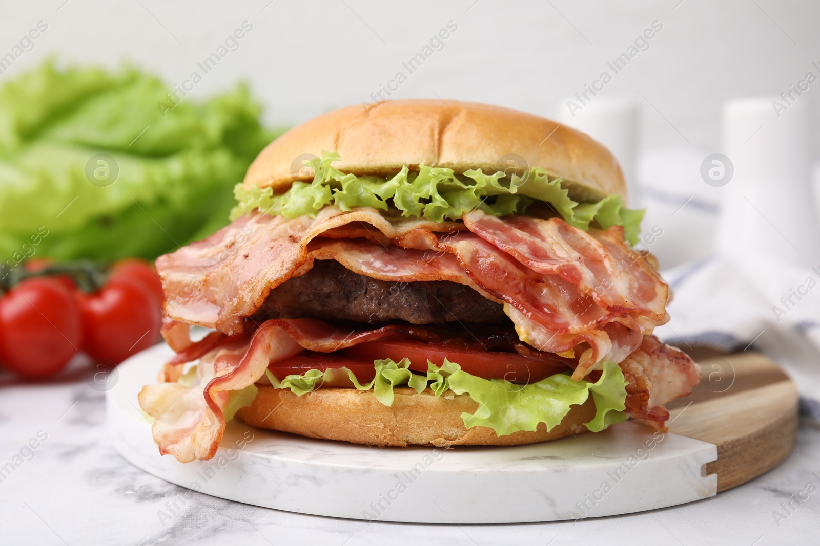 Photo of Delicious burger with bacon, patty and tomato on white marble table