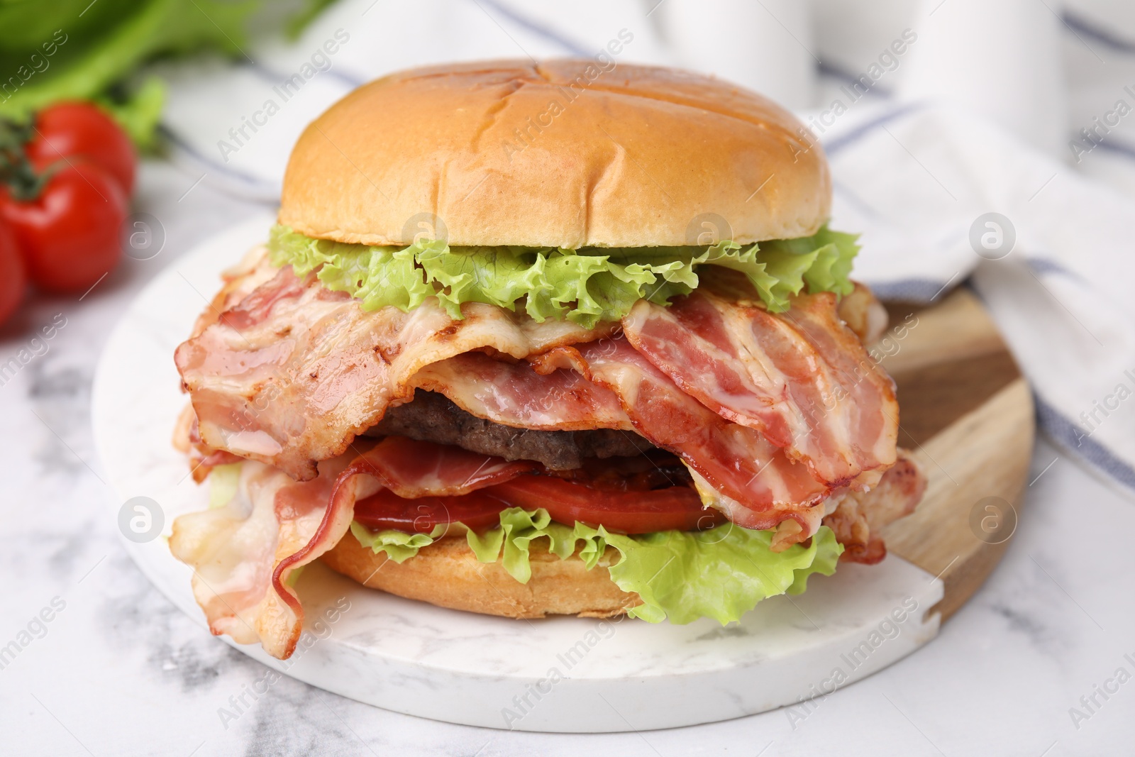 Photo of Delicious burger with bacon, patty and tomato on white marble table