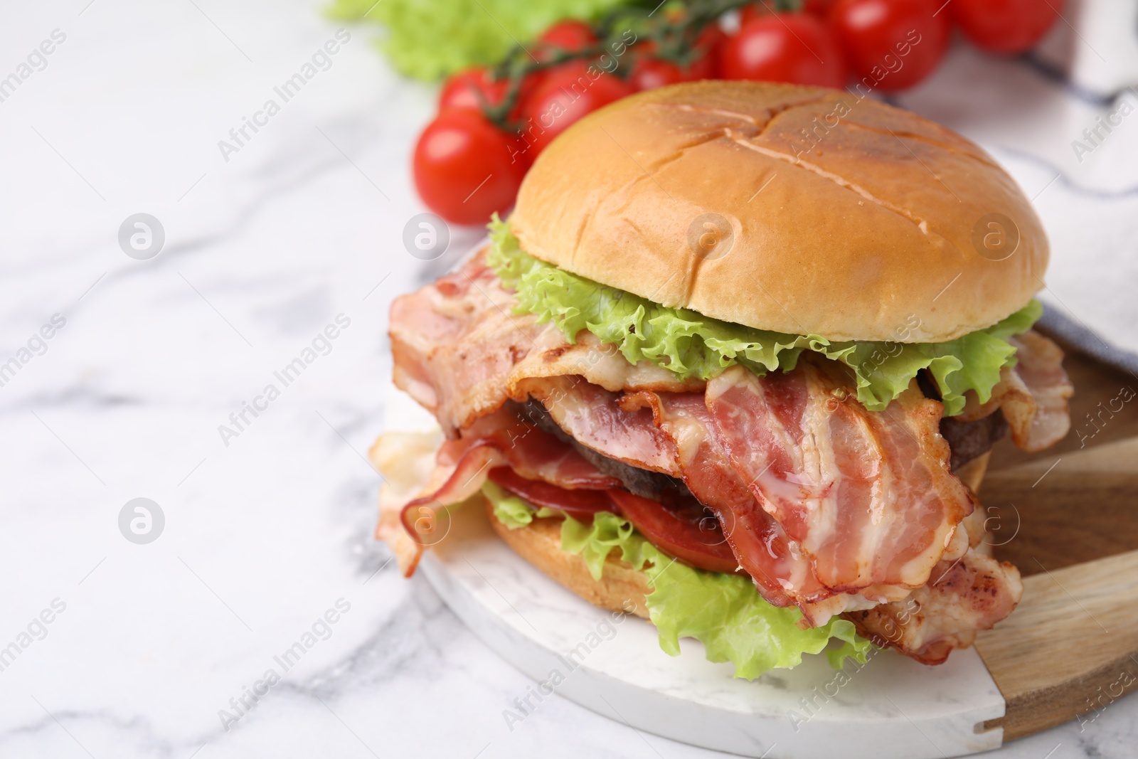 Photo of Delicious burger with bacon, patty and tomato on white marble table, space for text