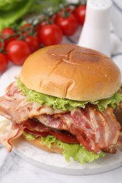 Photo of Delicious burger with bacon and tomatoes on white marble table