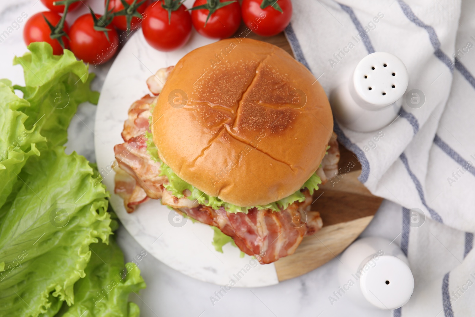 Photo of Delicious burger with bacon, lettuce and tomatoes on white marble table, top view