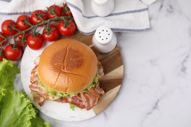 Photo of Delicious burger with bacon, lettuce and tomatoes on white marble table, top view. Space for text