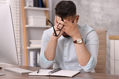 Overwhelmed man with glasses sitting at table in office