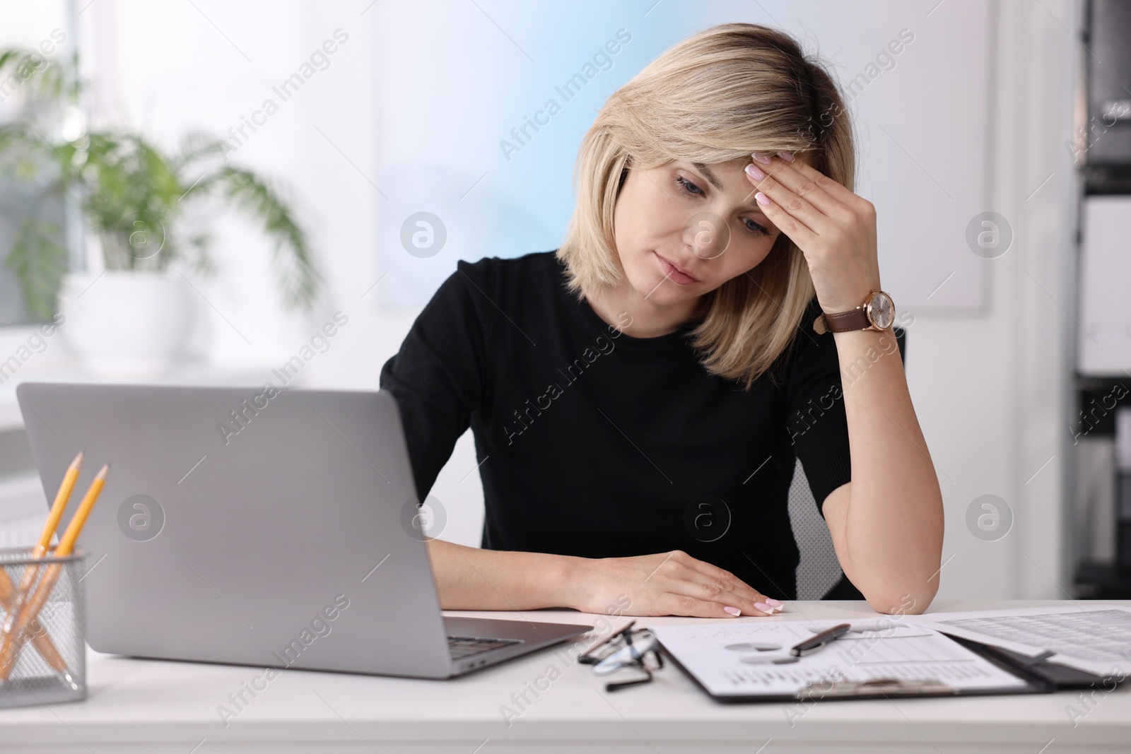 Photo of Overwhelmed woman sitting at table with laptop and documents in office