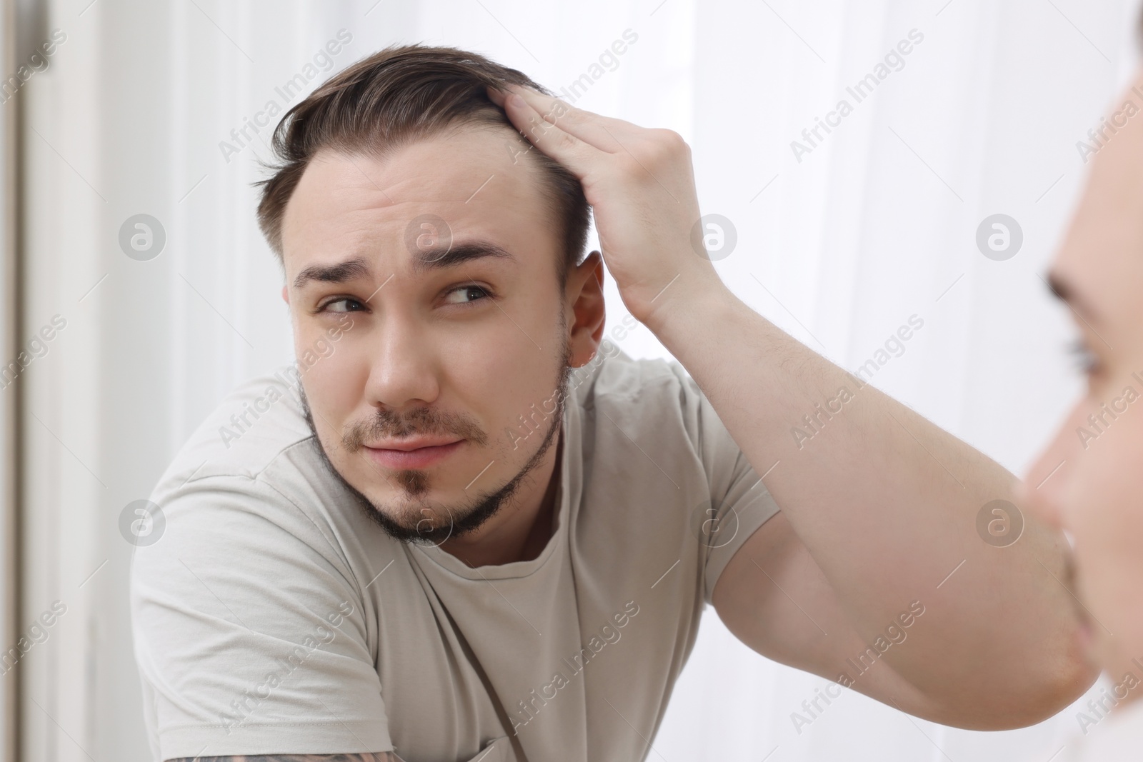 Photo of Baldness concept. Sad man with receding hairline looking at mirror indoors