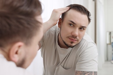 Baldness concept. Sad man with receding hairline looking at mirror indoors