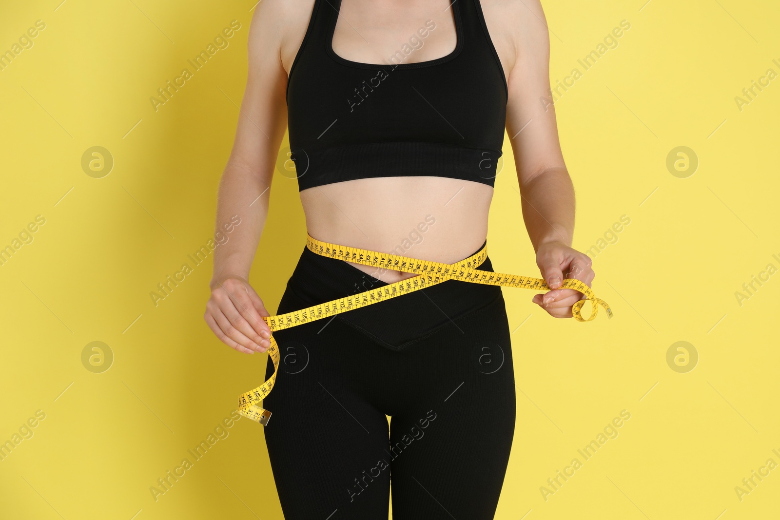 Photo of Woman with measuring tape showing her slim body against yellow background, closeup