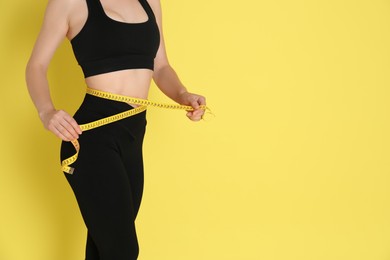 Woman with measuring tape showing her slim body against yellow background, closeup. Space for text