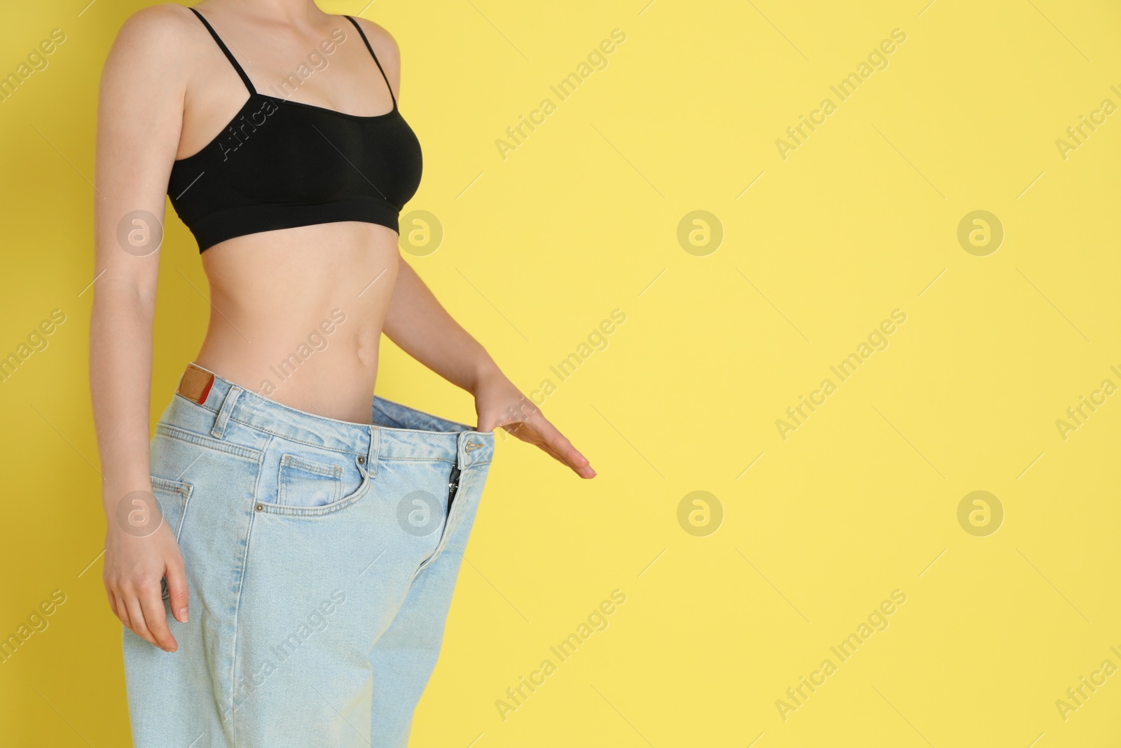 Photo of Woman in big jeans showing her slim body on yellow background, closeup. Space for text