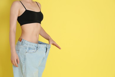 Photo of Woman in big jeans showing her slim body on yellow background, closeup. Space for text