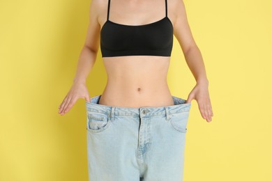 Photo of Woman in big jeans showing her slim body on yellow background, closeup