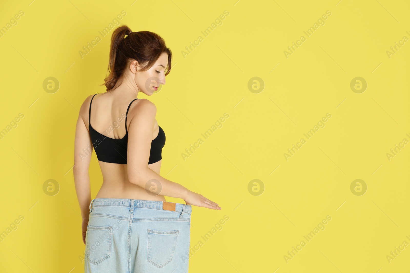 Photo of Woman in big jeans showing her slim body on yellow background, space for text