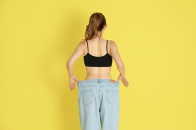 Woman in big jeans showing her slim body on yellow background