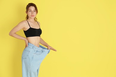 Photo of Woman in big jeans showing her slim body on yellow background, space for text