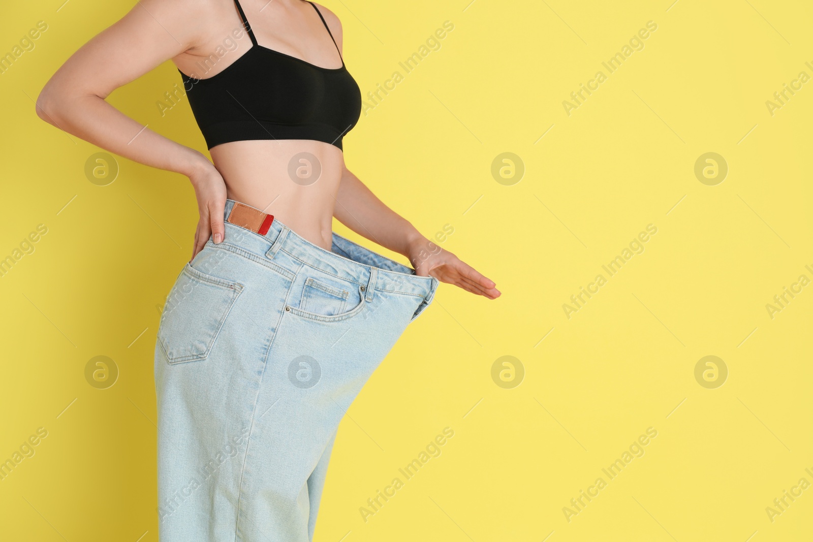 Photo of Woman in big jeans showing her slim body on yellow background, closeup. Space for text