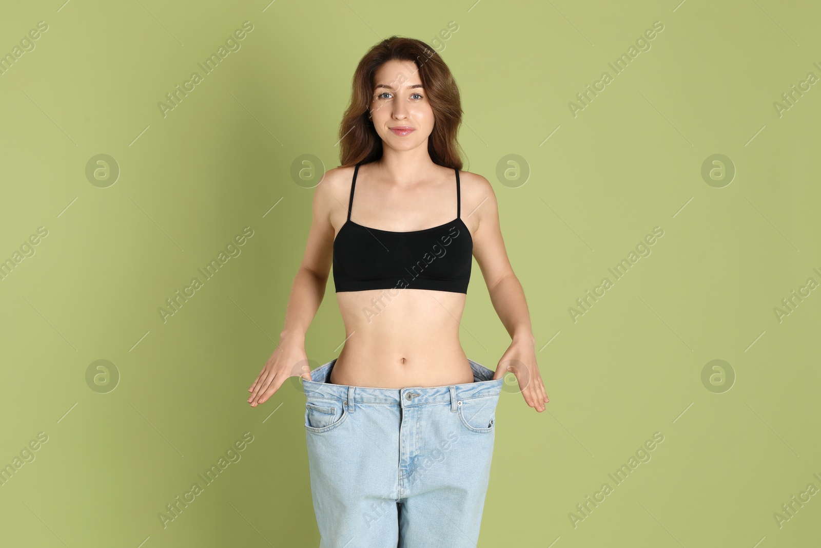 Photo of Woman in big jeans showing her slim body on olive background