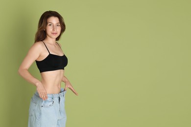 Photo of Woman in big jeans showing her slim body on olive background, space for text