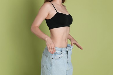 Photo of Woman in big jeans showing her slim body on olive background, closeup