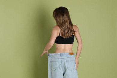 Woman in big jeans showing her slim body on olive background, back view