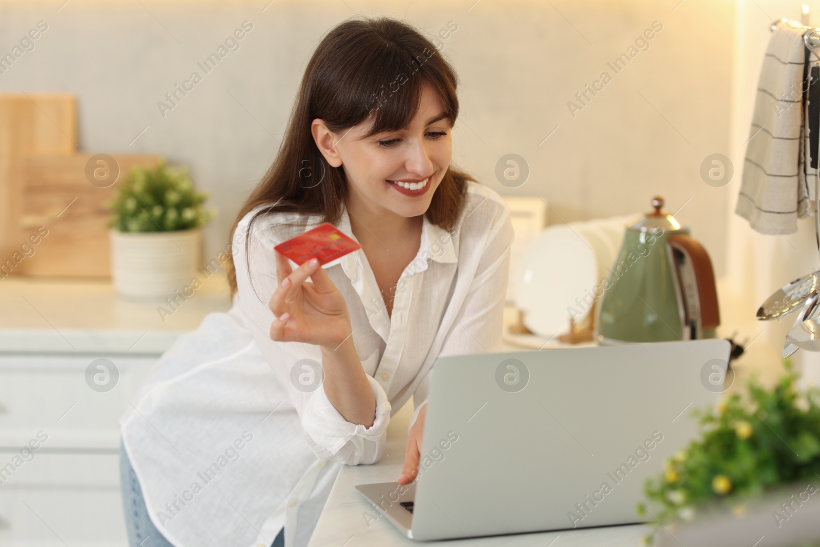 Photo of Online banking. Smiling woman with credit card and laptop paying purchase in kitchen