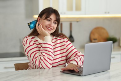 Online banking. Smiling woman with credit card and laptop paying purchase at table indoors