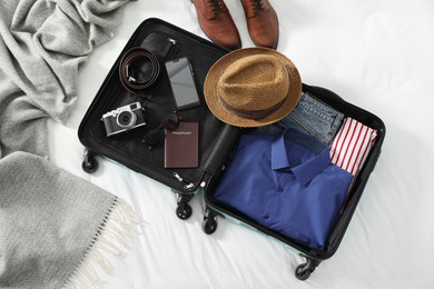 Open suitcase with traveler's belongings on bed, flat lay