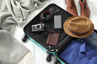 Open suitcase with traveler's belongings on bed, above view