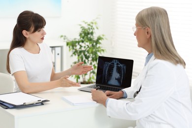 Photo of Lung cancer. Doctor showing chest x-ray on laptop to her patient in clinic