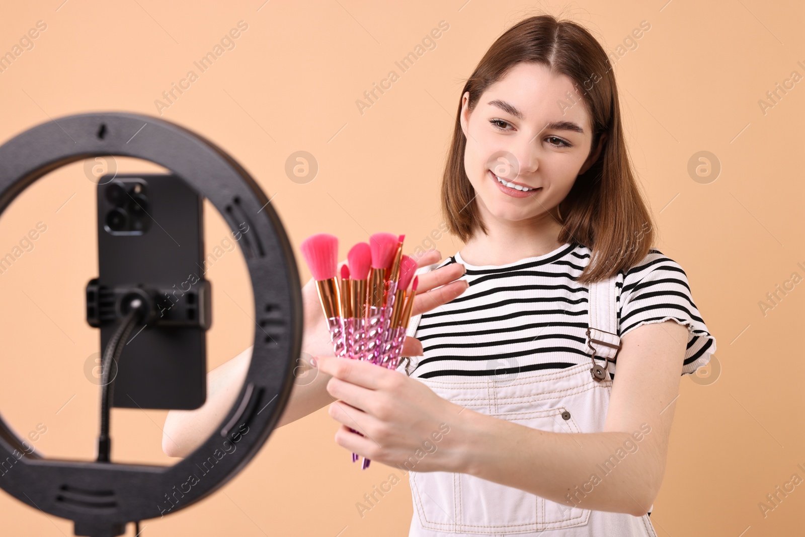 Photo of Beauty blogger reviewing makeup brushes and recording video with smartphone and ring lamp on beige background