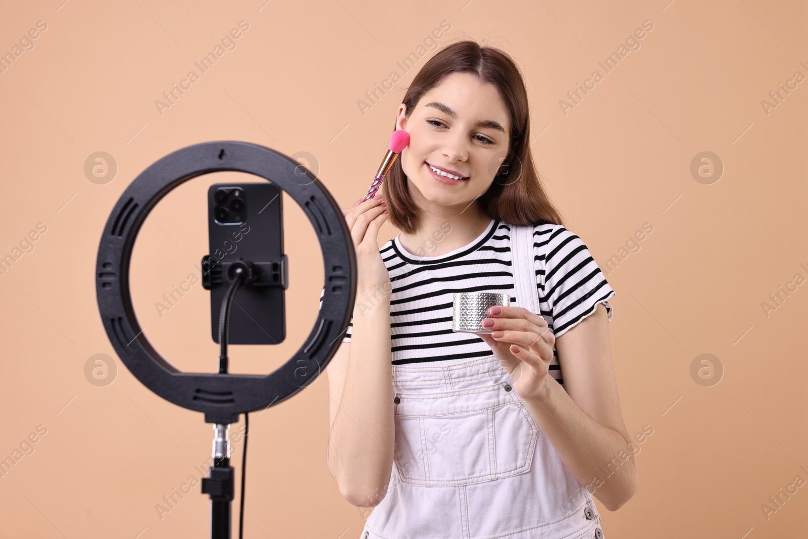 Photo of Beauty blogger reviewing decorative cosmetic product and recording video with smartphone and ring lamp on beige background