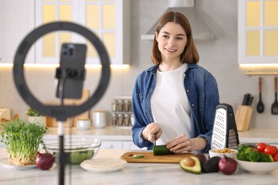 Food blogger cooking while recording video with smartphone and ring lamp in kitchen