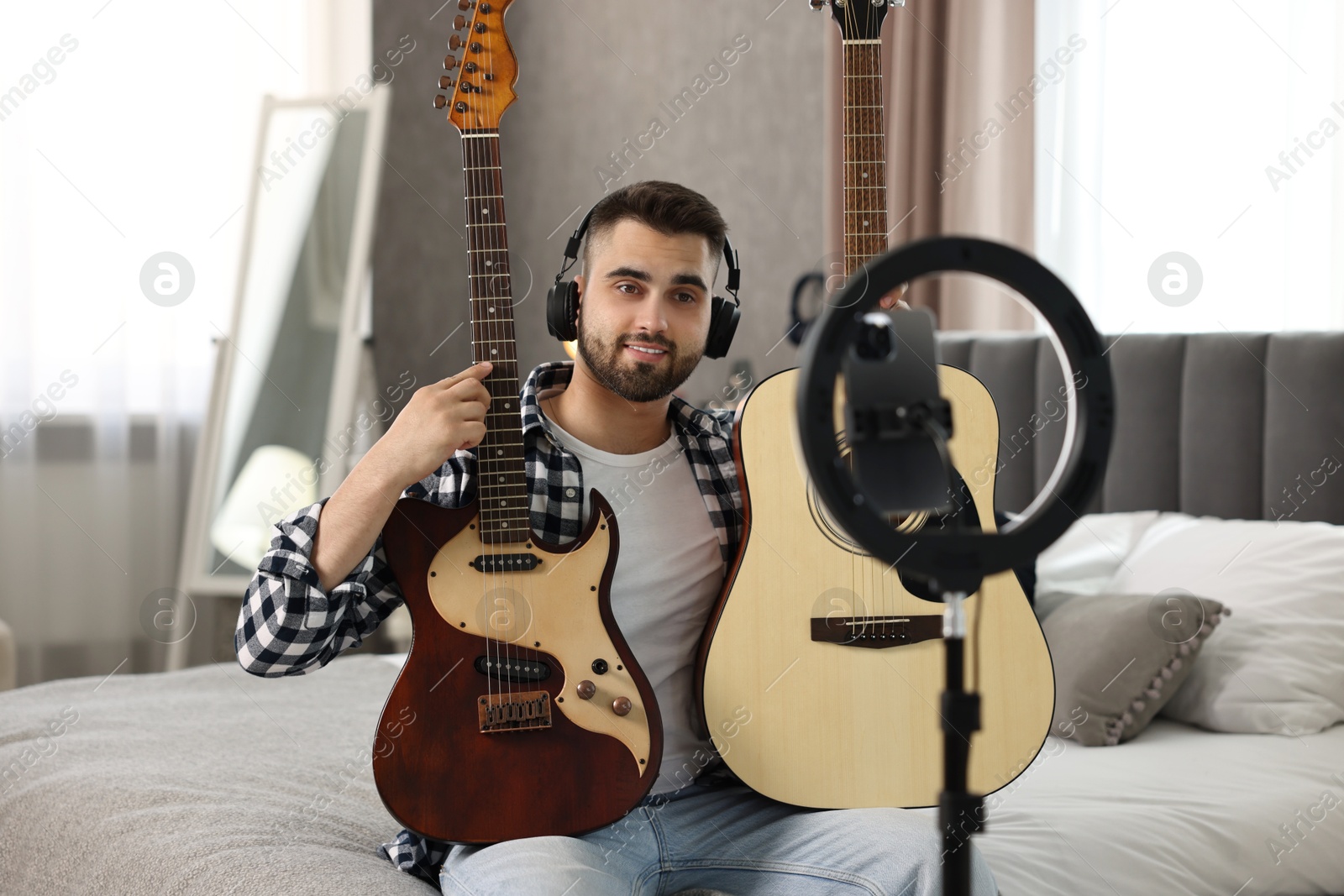 Photo of Music blogger recording guitar lesson with smartphone and ring lamp at home