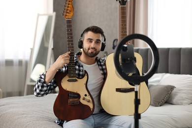 Photo of Music blogger recording guitar lesson with smartphone and ring lamp at home