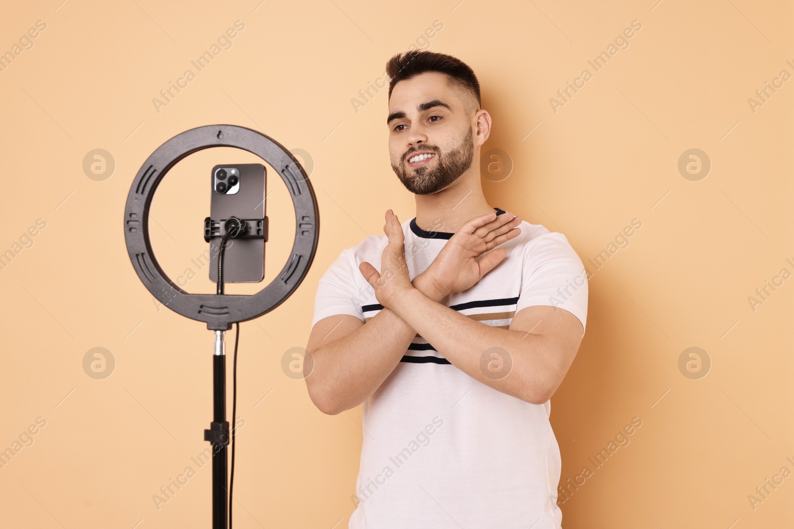 Photo of Blogger recording video with smartphone and ring lamp on beige background